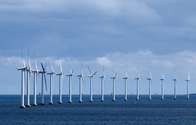 Long row of many wind turbines in the ocean.