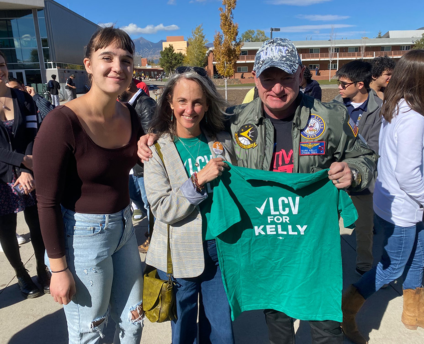 Two supporters stand with Senator Mark Kelly as he holds an "LCV for Kelly" shirt.