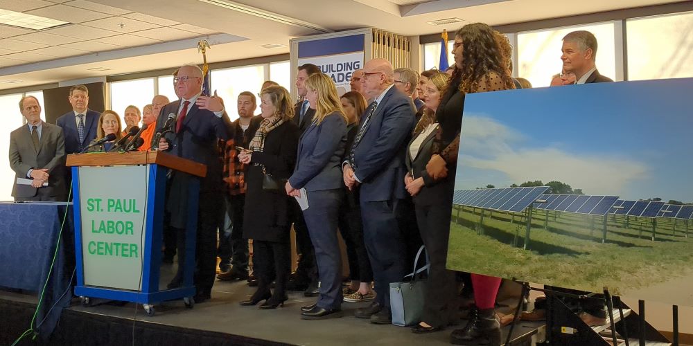 Minnesota Governor Tim Walz speaks at a podium with a group of activists on stage