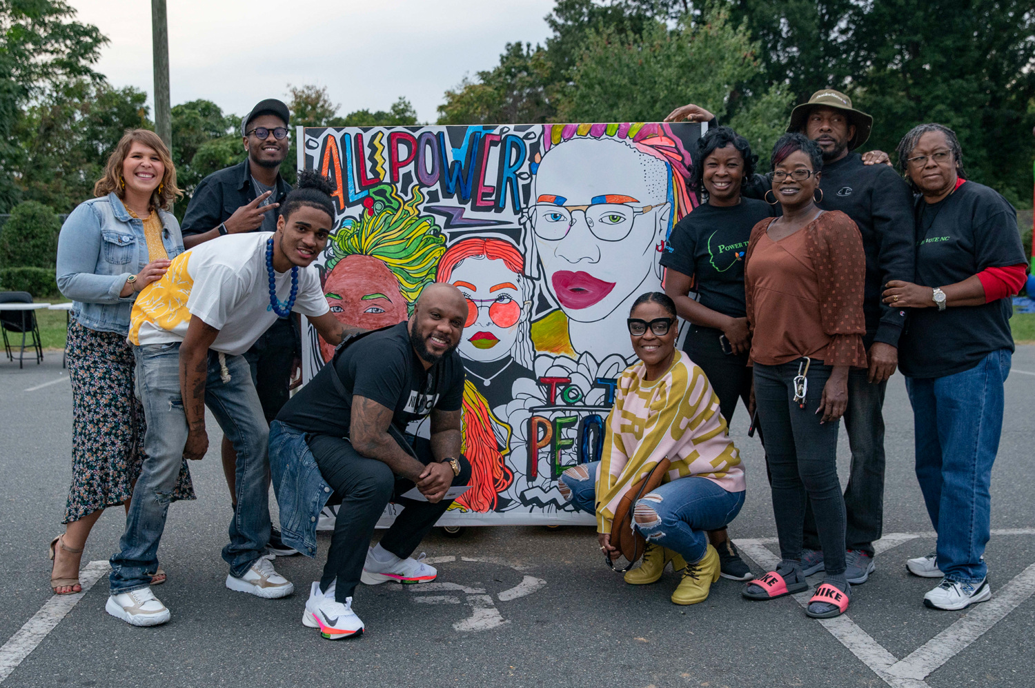 Group of people standing in front of an art installation that reads, "All Power to All People".