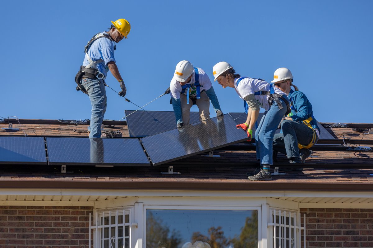 Clean Energy in Action: A team of four men and women install solar panels on the roof of a house.