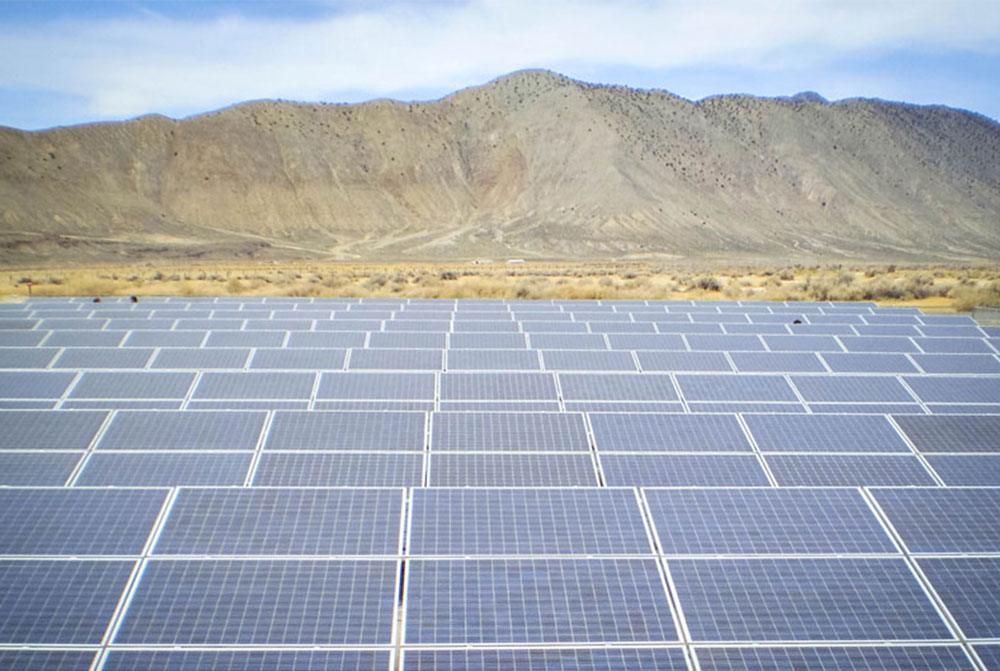 A field of solar panels in front of a mountain range in California.