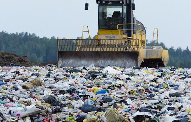 Bulldozer pushing piles of textile waste in a dump site.