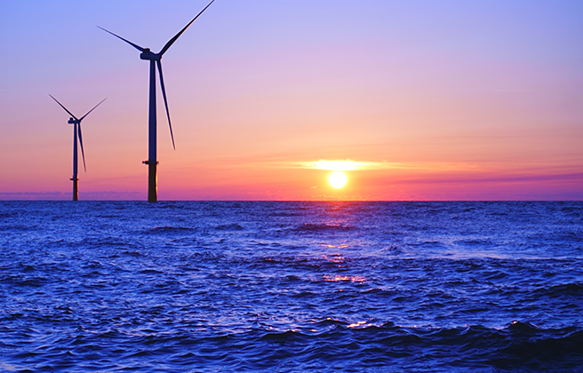 Sunset over an ocean horizon with wind turbines.